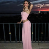 Woman in a pink outfit standing against a sunset sky.